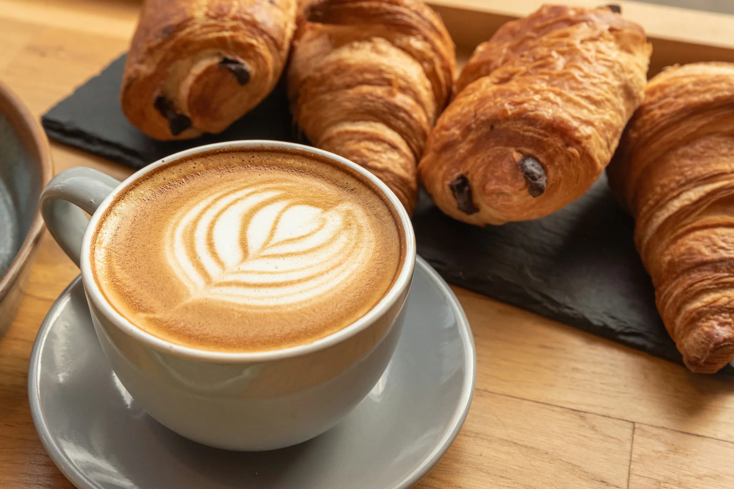 Cappuccino con latte art e cornetti su un vassoio di ardesia, su un tavolo di legno